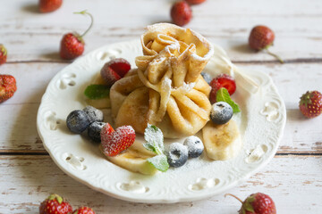 Delicate pancakes with fruits and berries on a wooden table.