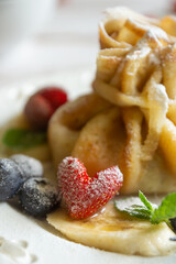 Delicate pancakes with fruits and berries on a wooden table.