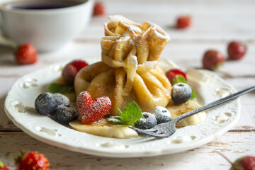 Delicate pancakes with fruits and berries on a wooden table.