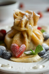 Delicate pancakes with fruits and berries on a wooden table.