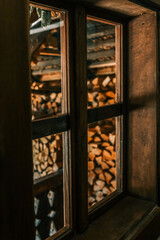 Warm light streams through a rustic wooden-framed window, reflecting neatly stacked firewood outside and casting cozy shadows across the vintage cabin interior