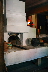 Traditional white clay hearth in a rustic cabin kitchen, glowing kerosene lantern, pottery and wooden utensils evoke a cozy sense of folk heritage