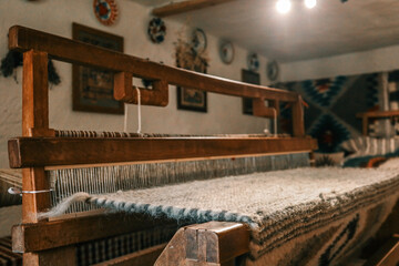 Handcrafted wooden loom with wool fabric partially woven, situated in cozy rustic interior with...