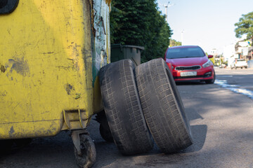 Two worn out tires with bald treads next to a yellow trash can © Mikhail