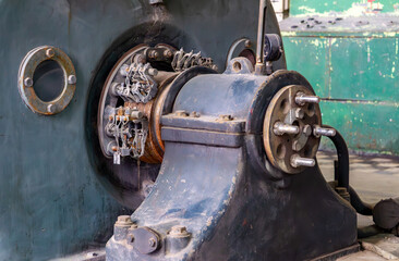 old industrial generator with exposed wiring and mounting bolts, set in a deteriorated factory interior. Vintage machinery with a strong industrial atmosphere.