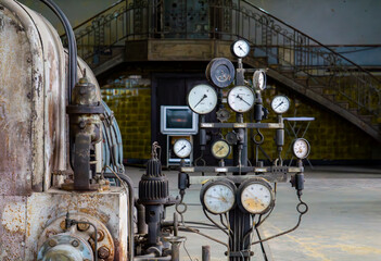 Vintage industrial equipment with a cluster of pressure gauges and pipes in an old factory hall....