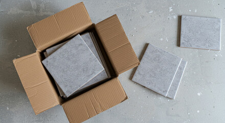 Cardboard box with ceramic tiles unpacked on grey floor  