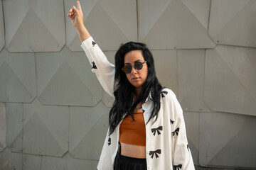 Young woman raising arm and making peace sign with fingers in front of modern building facade