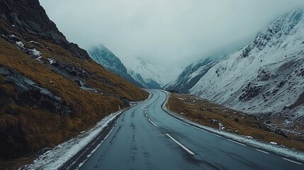 Winding road through a mountain pass, snow-capped peaks, overcast skies