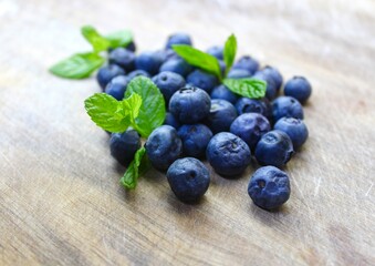 Close up of fresh blueberries with green mint leaves on rustic surface. 