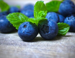 Close up of fresh blueberries with green mint leaves on rustic surface. 