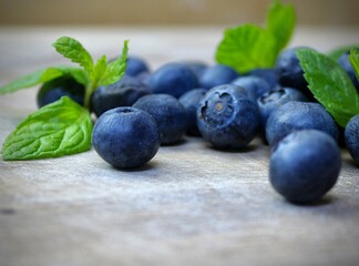 Close up of fresh blueberries with green mint leaves on rustic surface. 