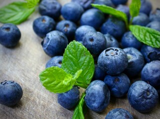 Close up of fresh blueberries with green mint leaves on rustic surface. 