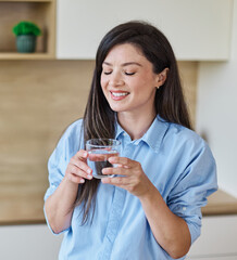 Portrait of a young woman gettyng ready for work drinking a glass of water for hydration standing...