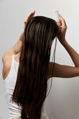 Long, shiny hair being styled with a comb against a light gray background The image captures a...