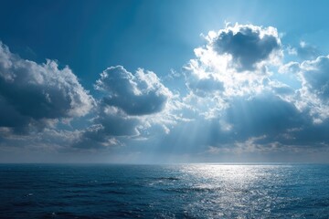 Obraz premium Sunbeams pierce fluffy cumulus clouds above a calm, deep blue ocean under a vibrant sky