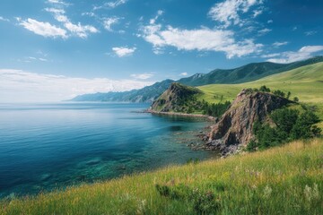 Fototapeta premium Serene coastal landscape featuring a rocky headland, clear turquoise water, rolling green hills under a vibrant blue sky with scattered clouds