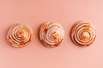 Top view of three delicious homemade sweet cinnamon rolls bun dessert glazed with sugar icing laying in a row on a pink brown background usually served for breakfast as freshly baked pastry snack