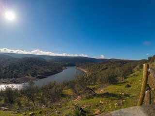  Scenic view of a reservoir in Monfragüe Natural Park, Extremadura, Spain. Bright sun over rolling hills and Mediterranean landscape.