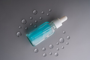 blue dropper bottle with serum on grey with waterdrops