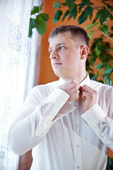 A man in a white shirt is getting dressed and fixing his collar