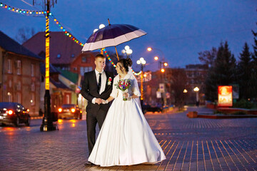 A bride and groom are walking down a street holding an umbrella