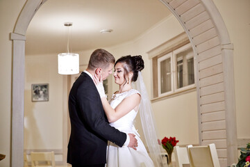 A bride and groom are embracing in a white wedding dress and suit