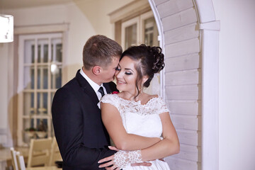 A bride and groom are hugging each other in a white dress and black suit