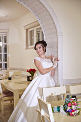 A woman in a white dress stands in front of a wall with a floral arrangement