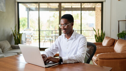 Fototapeta premium African American man working on laptop at desk in bright living room