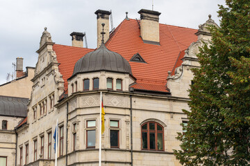 Historic European government building with ornate dome, red tile roof, brick chimneys and flags against cloudy sky. Classical architecture and administrative heritage landmark concept. 