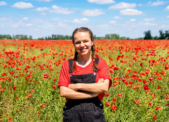 Confident female conservationist with arms crossed by rewilded field with red wild poppies.