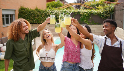 Happy diverse friends raising glasses with refreshing lemonade, enjoying summer party by swimming pool