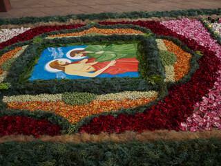 Vibrant floral carpet depicting Christ's deposition, meticulously crafted for Corpus Domini feast...