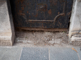 Weathered metal door edge revealing cracked concrete sidewalk, symbolizing urban deterioration and...