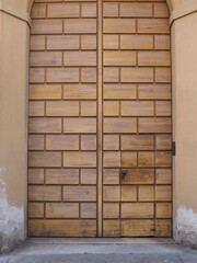 Closed wooden door resembling bricks, featuring a small pedestrian entrance and round metal handle, enhancing Cremona's rustic charm