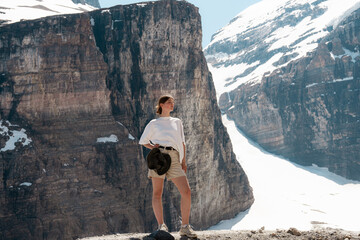 Woman stands surrounded by dramatic snowy cliffs and bright daylight.