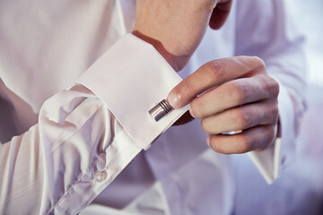 A man is getting dressed and putting on a cufflink