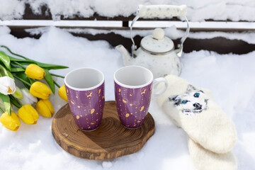 cups of hot tea on a park bench in the white snow. A teapot with a warming drink