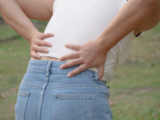 An Asian woman experiences back and hip pain while walking in the park—highlighting a health care...