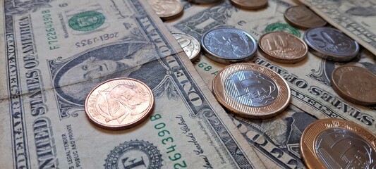 Close up of Brazilian real coins on top of dollar bills