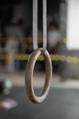 Naklejka premium Close-up of a single wooden gymnastics ring suspended from ceiling. Fitness equipment in a gym setting. Perfect for athletes and fitness enthusiasts.