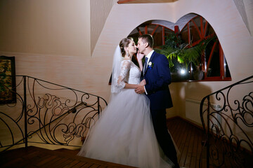 A bride and groom are kissing in front of a staircase