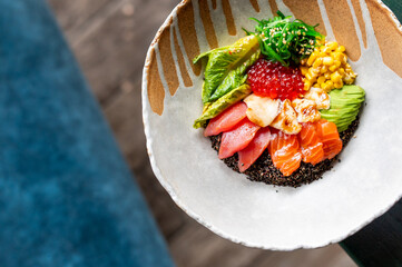 Colorful poke bowl with salmon, tuna, avocado, corn, seaweed salad, fish roe, and black quinoa in a...