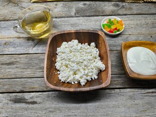 Homemade traditional cottage cheese organic dairy product in wooden bowl, next to it is a cup of sour cream