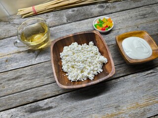 Homemade traditional cottage cheese organic dairy product in wooden bowl, next to it is a cup of...
