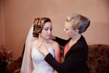A woman in a wedding dress is being helped by another woman