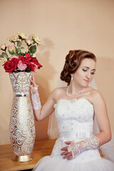 A woman in a white dress sits in front of a vase of red flowers