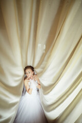 A bride is standing in front of a curtain, looking at the camera