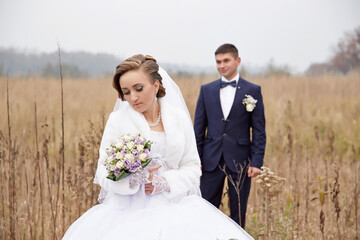 A bride and groom are standing in a field with a bouquet and a boutonniere